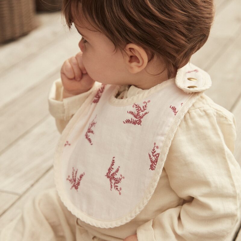 Bavoir bébé avec motif floral rouge, porté par un enfant assis.